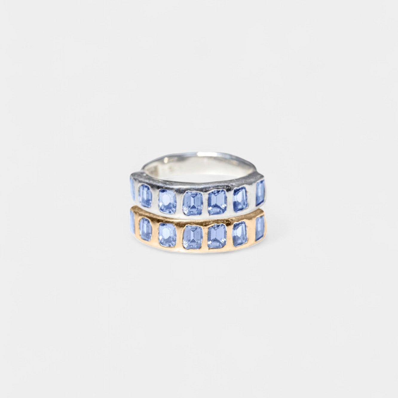 A double-row ring featuring rectangular light blue gemstones in silver and gold settings, centered on a light gray background.